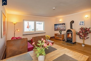 Una sala de estar acogedora con chimenea, un sofá, una mesa de comedor con un jarrón de flores y un ventanal grande.