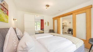 A bedroom with a bed, a sofa, a mirror, and a sliding door leading to a kitchen. - Ferienwohnung Kranich (Heringsdorf)