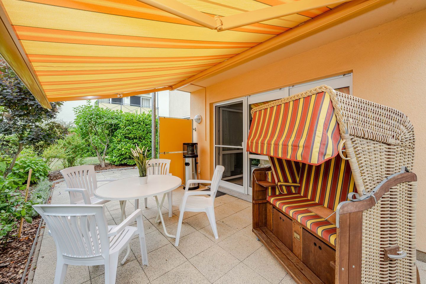 An outdoor patio with a table and chairs, a wicker sofa, and a striped awning.
