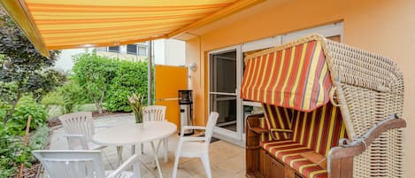 Une terrasse extérieure avec une table et des chaises, un canapé en osier et un auvent à rayures.