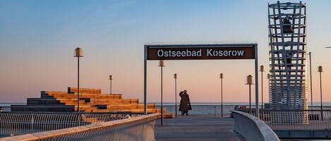 A pier with a sign reading 'Ostseebad Koserow,' benches, and a person walking.