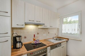 A compact kitchen with a built-in oven, a coffee maker, and a wine bottle on the counter.