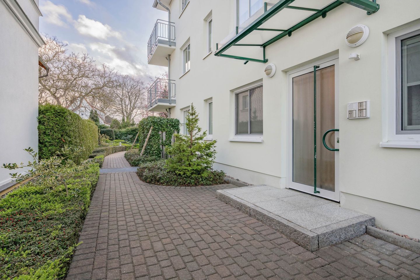 Ein Wohngebäude mit einem gepflasterten Weg, einer Tür mit Fensterteil und einem kleinen Garten.