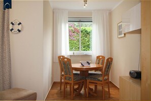A dining area with a round wooden table and four chairs, a window with curtains, a life preserver on the wall, and a radio on a cabinet. - Ferienwohnung Ferienidyll 1 - Tolle Ferienwohnung in Strandnaher Lage mit Terrasse, Wlan und (Heringsdorf)