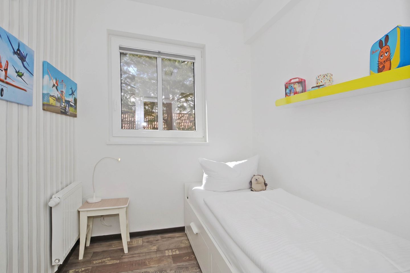 Ein Zimmer mit einem Bett, einem kleinen Tisch, einem Heizkörper, einem Fenster und Wanddekorationen.