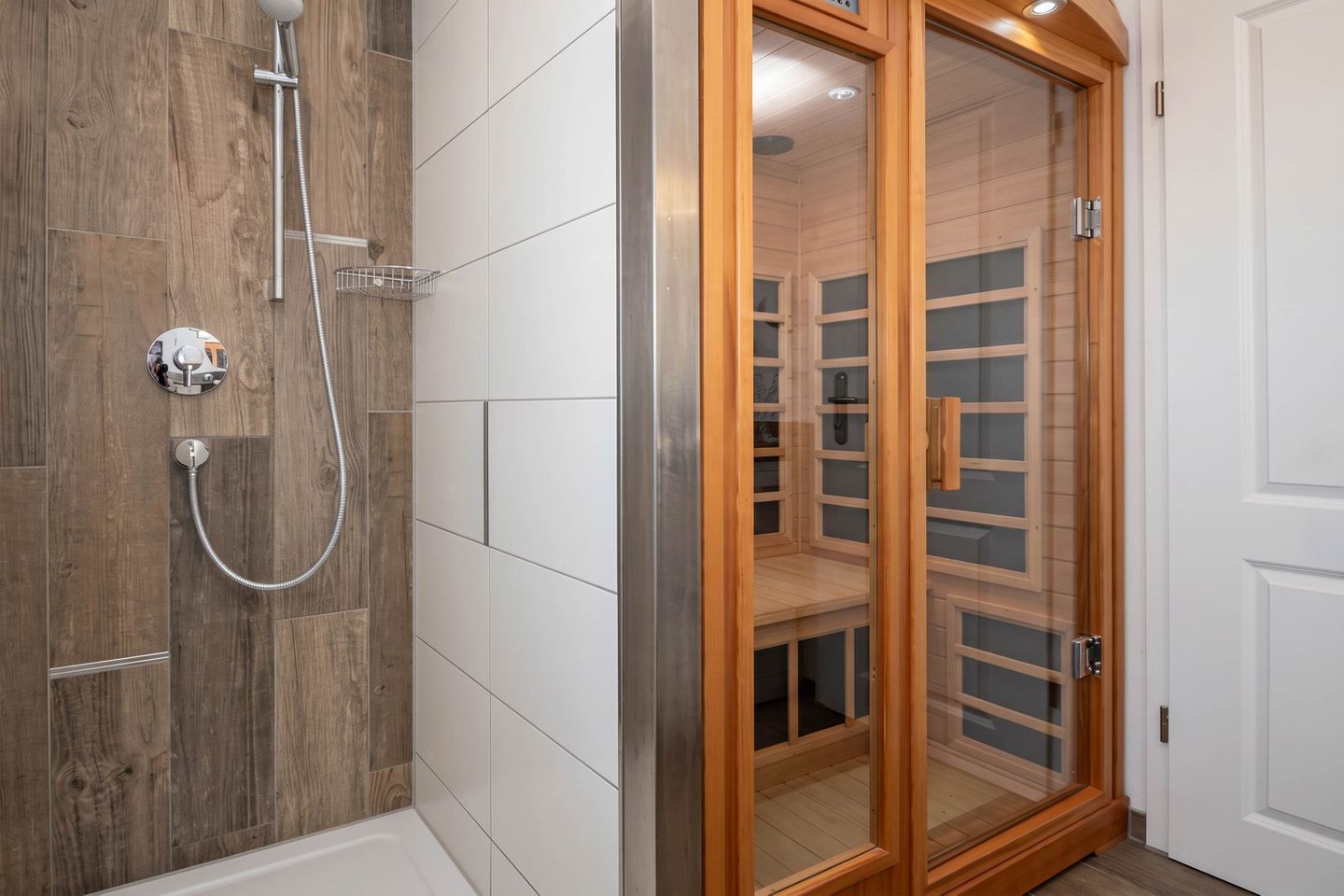 A bathroom with a wooden shower enclosure, a glass door, and a white tiled wall.