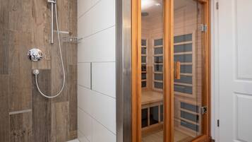 A bathroom with a wooden shower enclosure, a glass door, and a white tiled wall.