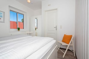 Ein Schlafzimmer mit einem Bett, einem Sessel, einem Fenster und einer Tür.