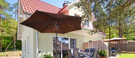Una casa con patio, mobiliario exterior y un gran paraguas.