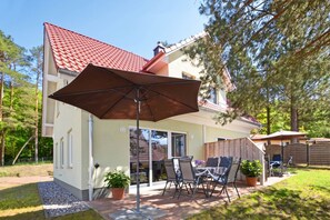 Et hus med terrasse, udendørs møbler og en stor parasol.
