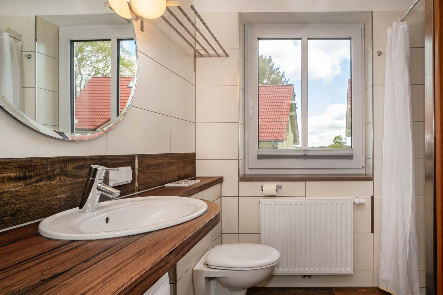 Ein Badezimmer mit einem Holzkosmetikschrank, einem weißen Waschbecken, einem Spiegel, einem Fenster und einer weißen Toilette.