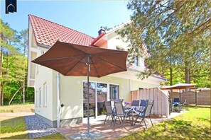 A house with a patio area featuring a table and chairs, a large umbrella, and a red-tiled roof.