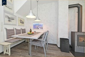 A modern kitchen with a dining area, featuring a white table, grey chairs, a bench, pendant lights, and a built-in stove.