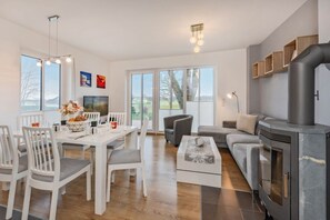 A modern living room with a fireplace, dining area, and large windows. - DHH Anemone - Gemütliche Doppelhaushälfte für bis zu 6 Personen, mit Kamin und Terrasse (Korswandt)