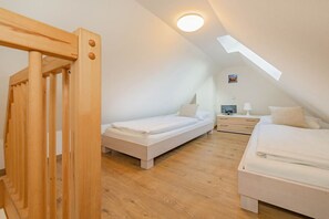 A bedroom with two beds, a wooden staircase, a ceiling light, and a small bedside table with a lamp. - DHH Anemone - Gemütliche Doppelhaushälfte für bis zu 6 Personen, mit Kamin und Terrasse (Korswandt)