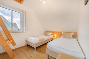 Ein kleines, helles Schlafzimmer im Dachgeschoss mit einem Schlafplatz in der Zwischengeschoss-Konstruktion, einem Einzelbett und einer Holzleiter.