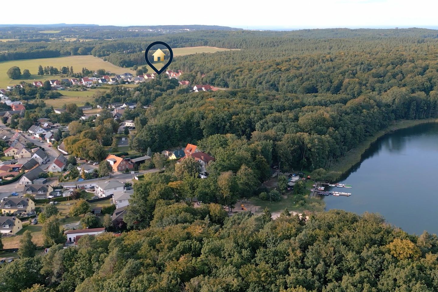 Ein Luftbild eines Wohngebiets mit Häusern, einem See und bewaldeter Landschaft.