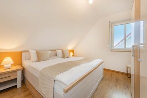 A bedroom with a bed, bedside tables, a window, and a view of the outside. - DHH Anemone - Gemütliche Doppelhaushälfte für bis zu 6 Personen, mit Kamin und Terrasse (Korswandt)