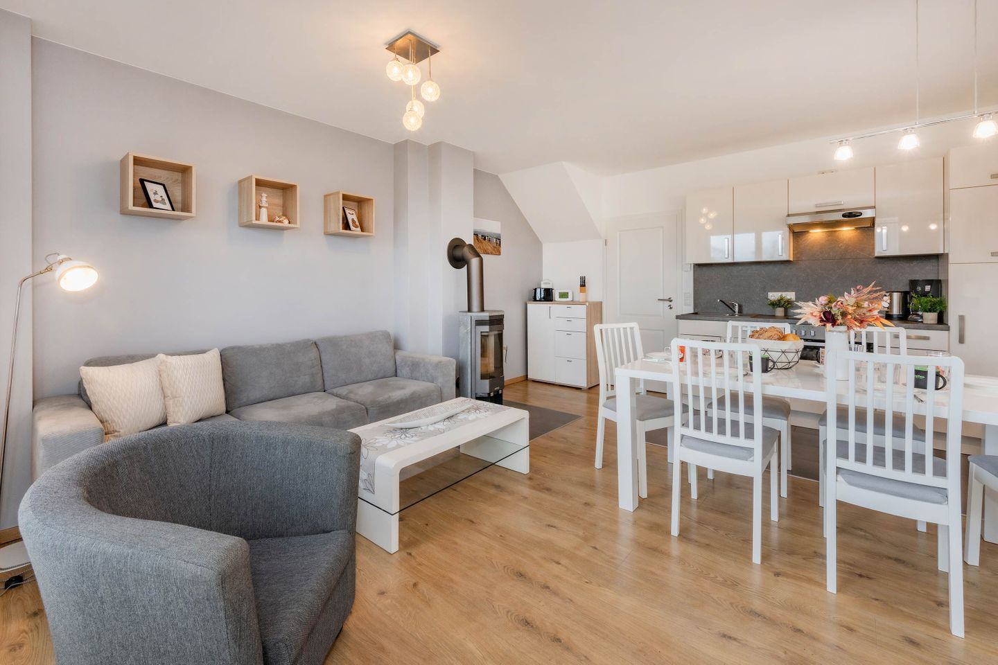 Een moderne woonruimte met een grijze bank, een witte eettafel en stoelen.