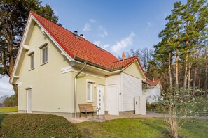 A two-story house with a red-tiled roof, a front door, and a small bench outside. - DHH Anemone - Gemütliche Doppelhaushälfte für bis zu 6 Personen, mit Kamin und Terrasse (Korswandt)