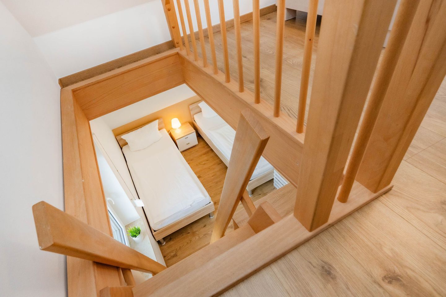 A wooden staircase leading to a bedroom with a bed, bedside table, and lamp.