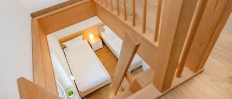 Una escalera de madera conduce a un dormitorio con cama, mesita de noche y lámpara.