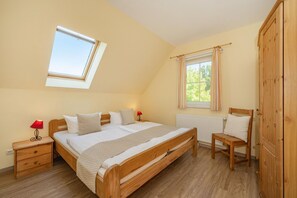 Ein Schlafzimmer mit schrägverdeckter Decke, einem Oberlicht, einem Bett mit weißer Bettwäsche, einem Nachttisch mit Lampe, einem Sessel und einem Kleiderschrank.