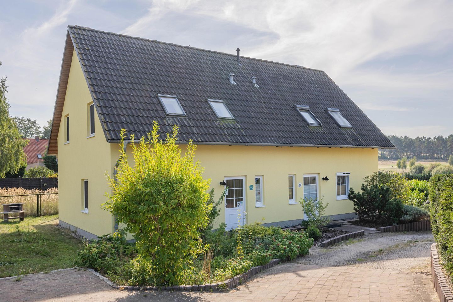 Une maison à deux étages, avec un toit en pente, de nombreuses fenêtres et une allée pavée.