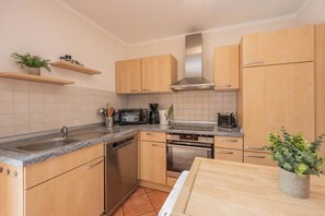 Eine kompakte Küche mit Holzausstattung, einer Edelstahl-Dunstabzugshaube, einem Geschirrspüler, einem eingebauten Backofen und einer Arbeitsplatte aus Granit.
