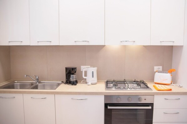 Una cocina moderna con armarios blancos, un fregadero, una cafetera, un tostador y una estufa.