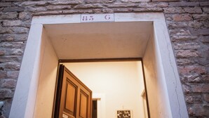 Ein Durchgang mit einem Schild, auf dem "85 G" steht, der in einen Raum mit einer Holztür und einem kleinen, gerahmten Bild an der Wand führt.