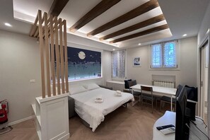 Un dormitorio moderno con cama, escritorio y ordenador. Se ve una ventana con vista a la ciudad.