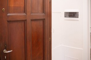 Uma porta de madeira com maçaneta e fechadura, e uma parede branca com painel de controle do termostato.