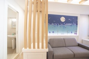Un salón moderno con un sofá gris, un panel divisor de madera y un cuadro con vista a la ciudad.