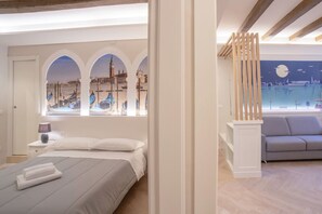 A bedroom with a bed, a nightstand, a lamp, and a window with a view of boats and buildings.