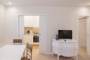 Um espaço de estar compacto com cozinha compacta, área de refeições e televisão sobre um aparador branco.
