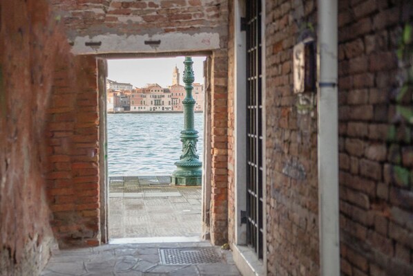 A narrow alleyway with a view of a canal and buildings in the background.