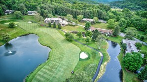 Ein Golfplatz mit Teich, Fluss und Häusern in einem bewaldeten Gebiet.