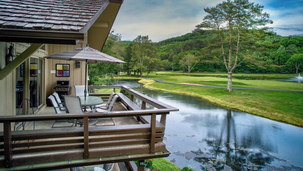 Eine HolzdTerrasse mit Gartenmöbeln, mit Blick auf einen Fluss und einen Golfplatz.