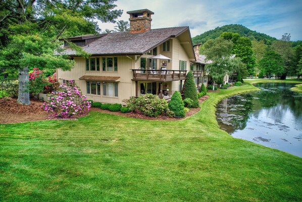 Situated beside a calm lake, this house offers a serene setting with a balcony, lush greenery, and a well-maintained lawn.