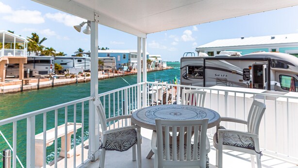 A covered outdoor area with a table and chairs, overlooking a marina with boats and a waterway.