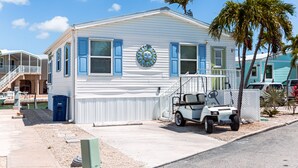 A white mobile home with blue shutters, a small porch, and a golf cart parked in front.