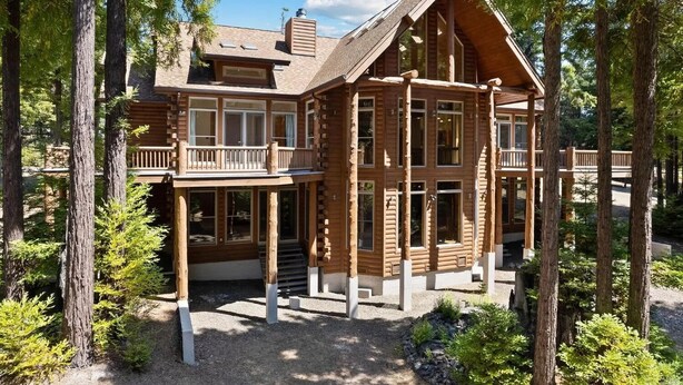 Une cabane en rondins dotée d’un balcon, de grandes fenêtres et d’une cheminée.
