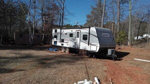 Un camping-car Coleman était stationné dans une zone boisée, à proximité d’un petit abri de jardin.