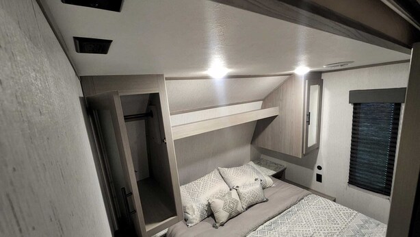 Une chambre à coucher de taille réduite, avec un lit superposé, une petite table de chevet et une fenêtre avec des stores.