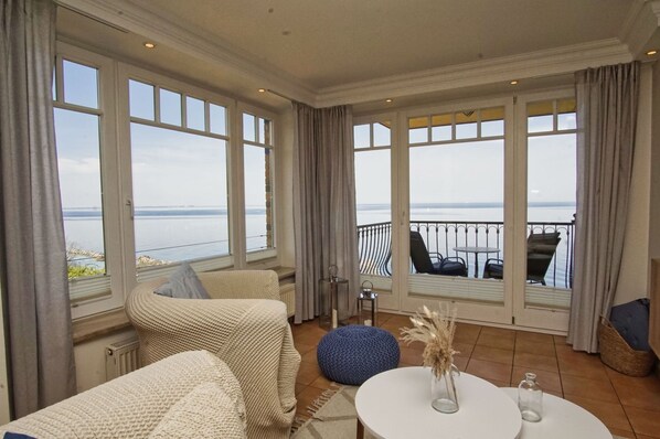 A spacious balcony with a view of the sea, furnished with a sofa, chairs, and a small table.