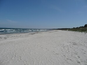 Ein weiter Sandstrand mit Fußspuren, ein klarer Himmel und eine entfernte Küstenlinie.