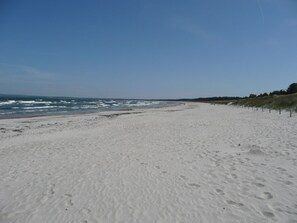 A wide sandy beach with footprints, a clear sky, and a distant shoreline.