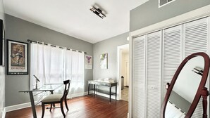 A room with a wooden floor, a desk with a chair, a mirror, and a wardrobe with louvered doors. - Broad Ripple 1 Bedroom  (Indianapolis)