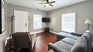 A living room with a ceiling fan, two grey sofas, a patterned armchair, a television, and a lamp. - Broad Ripple 1 Bedroom  (Indianapolis)